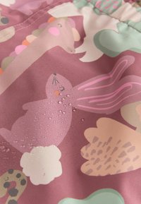 Wasserabweisender Stoff mit einem pinkfarbenen Hintergrund und verschiedenen Tier- und Blumenmustern, einschließlich eines Kaninchens mit Tropfen auf der Oberfläche.