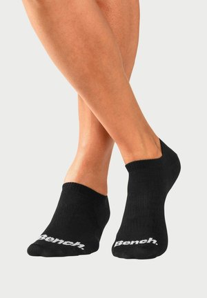 Chaussettes noires à chevilles en tissu extensible, avec un design court et un logo "Bench." blanc sur la zone des orteils. Texture lisse, style polyvalent.