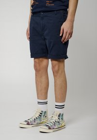 Pantalones cortos de algodón azul marino con dobladillos enrollados, combinados con calcetines de rayas blancas y deportivas multicolores de caña alta.