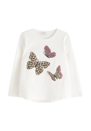 Chemise blanche à manches longues avec trois grands papillons sur le devant ; l'un a un motif léopard, les deux autres sont rosés et dorés.