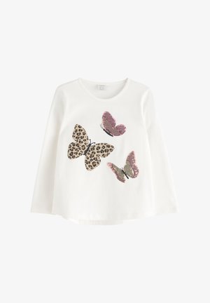Chemise blanche à manches longues avec trois grands papillons sur le devant ; l'un a un motif léopard, les deux autres sont rosés et dorés.