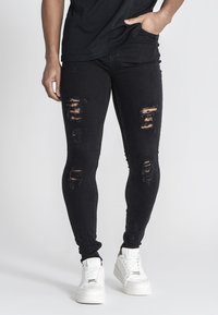 Musta farkkushortsit, joissa on kulutettuja reikiä, tiukka muotoilu ja hieman joustavaa materiaalia. Yhdistettynä valkoisiin lenkkareihin kontrastin luomiseksi.