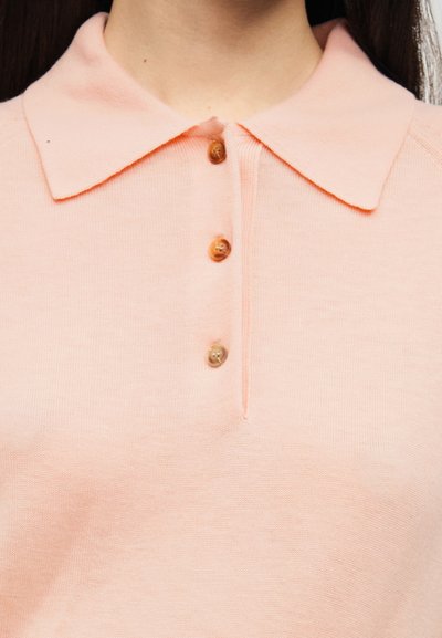 Πόλο πουκάμισο σε ροδακινί απόχρωση κατασκευασμένο από μαλακό ύφασμα, με γιακά, πέντε κουμπιά στο μπροστινό μέρος και ελαφριά υφή.