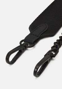 Cinghia nera in nylon con superficie texturizzata, dotata di due clip in metallo e un attacco a catena. Design utilitario con materiali resistenti.
