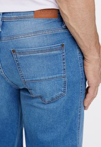 Jasnoniebieskie dżinsy z kontrastującym brązowym przeszyciem, z tylną kieszenią i brązową skórzaną metką z wytłoczonym napisem "JACK'S."