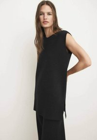 Top negro sin mangas hecho de una tela texturizada, con cuello redondo, aberturas laterales y un dobladillo recto. Combinado con pantalones negros a juego.