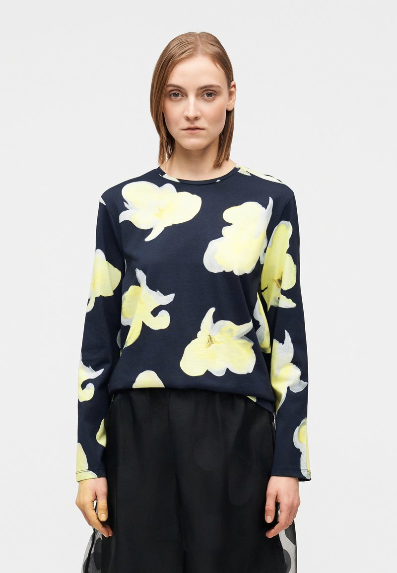 Μπλε σκούρο μπλούζα με μακριά μανίκια που διαθέτ�ει μεγάλα κίτρινα λουλουδάτα σχέδια, στρογγυλή λαιμόκοψη και ελαφρώς φαρδιά γραμμή, σε συνδυασμό με μια μαύρη φούστα.