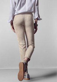 Beige suede legging in een enkellange snit, gecombineerd met zilveren schoenen en gebreide sokken, gezien vanaf de achterkant. Eenvoudige, gladde textuur.