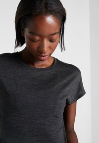 Dark gray, short-sleeve t-shirt with a crew neckline and a soft texture, worn by a person looking slightly downward.