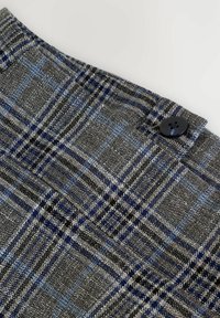 Grau und blau kariertes Gewebe mit strukturierter Oberfläche, das einen kleinen schwarzen Knopf und strukturierte Nähte aufweist. Nahaufnahme.