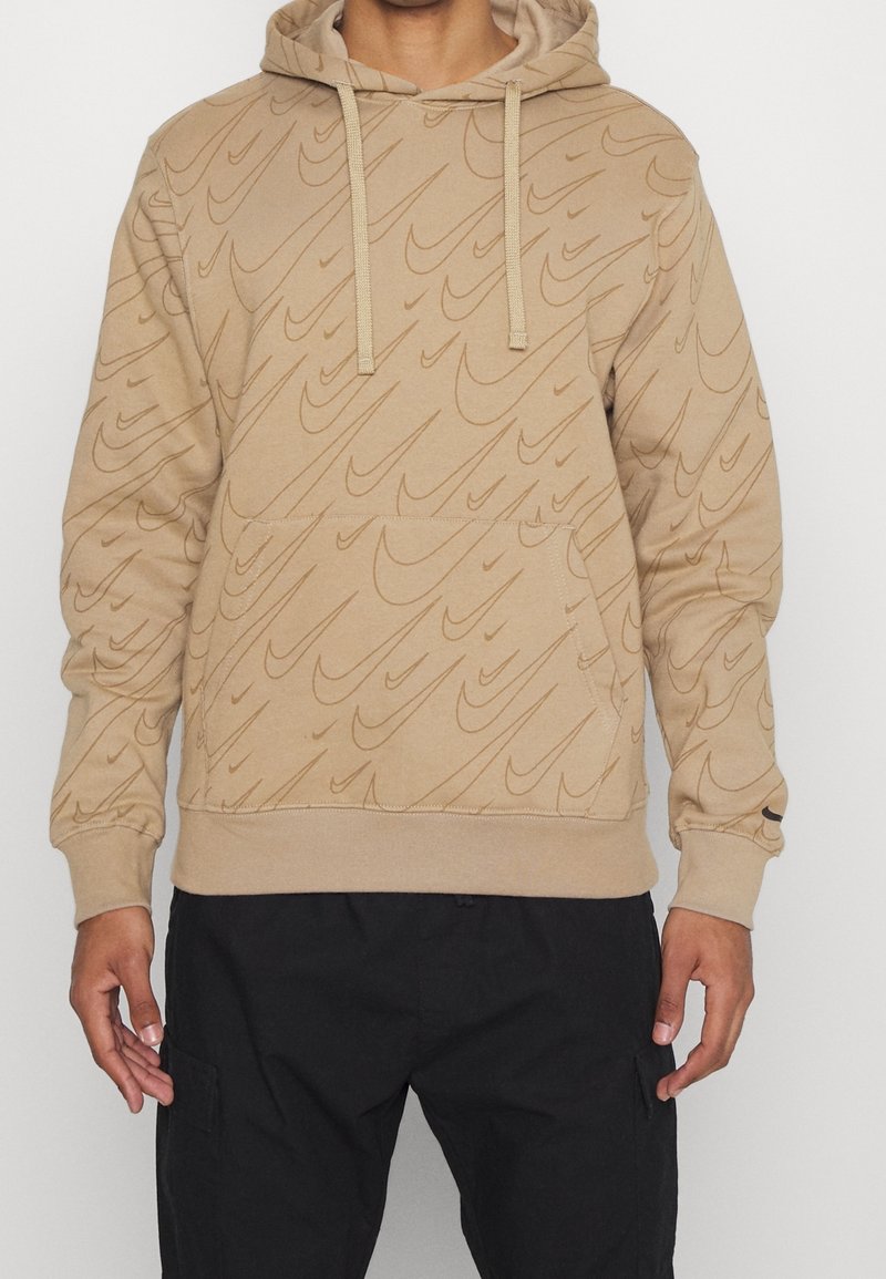 Beige hoodie med ett strukturerat vågmönster, dra snören och en framficka. Tillverkad av mjukt material med ribbade muddar och nederkant.