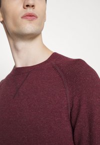 Bordeaux-Pullover mit strukturiertem Strickdesign, runder Ausschnitt und Raglanärmeln. Glatte, weiche Stoffqualität mit dezenten Details.