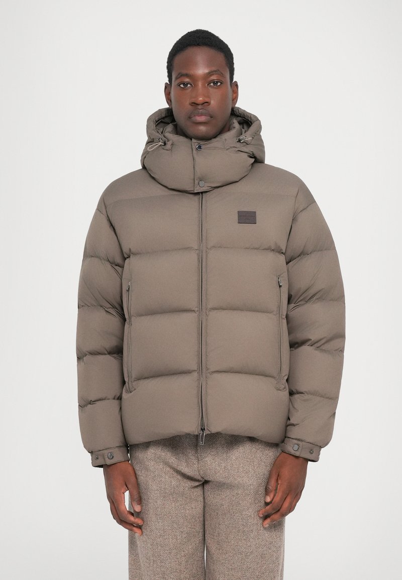 Puffer jacket in muted taupe, featuring a detachable hood, zip closure, and snap buttons. Horizontal quilted pattern with side pockets.