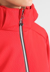 Rød lynlåstrøje med tekstureret mønster, høj krave og sort lynlås med hvide detaljer. Overfladen har en glat finish og subtil glans.