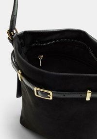 Borsa a secchiello in suede nero con tracolla in pelle regolabile, fibbia dorata e tasca interna con zip visibile dall'alto.