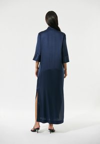 Abito lungo blu navy realizzato in tessuto morbido, con maniche a tre quarti, spacchi laterali e un design del colletto semplice.
