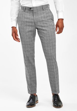 Homme portant un pantalon de costume gris à carreaux avec des poches avant, associé à des chaussures de ville en cuir noir et une chemise blanche.