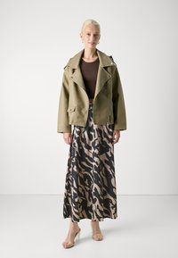 Olive green faux leather biker jacket with silver hardware, paired with a beige and black patterned maxi skirt and clear heeled sandals.