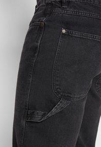 Svarta denimjeans med en närbild som visar sömnadsdetaljer, en slim fit-form och en sidoficka med en subtil textur.
