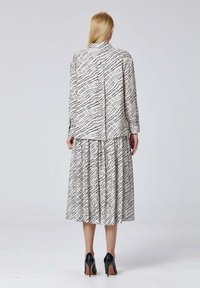 Robe imprimée avec une jupe plissée, arborant un motif abstrait noir et blanc, des manches longues et une fermeture à boutons au dos. Escarpins noirs.