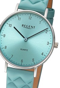 Montre en quartz de couleur aqua avec un cadran lisse et mat et des accents argentés. Bracelet en silicone turquoise matelassé. Boîtier en métal rond.