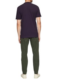 Dunkelviolettes T-Shirt mit kurzen Ärmeln, kombiniert mit olivgrünen, schmal geschnittenen Hosen, die elastische Bündchen und Seitentaschen aufweisen. Weiße Sneakers runden das Outfit ab.