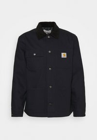 Blaue Arbeitsjacke mit einem Cordkragen, mehreren Fronttaschen, metallenen Druckknöpfen und einem sichtbaren Logopatch auf der linken Brusttasche.