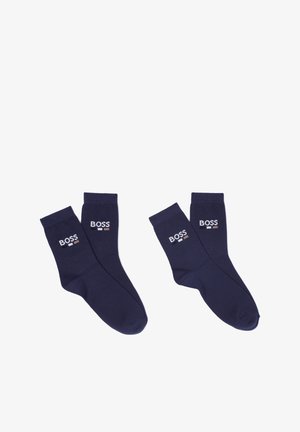 Chaussettes en coton bleu marine avec bords côtelés, arborant un logo "BOSS" brodé en blanc et des rayures d'accent. Texture lisse et longueur standard.