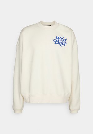 Sweat-shirt écru col rond avec manches longues et texte bleu "Wrst Bhvr" sur la poitrine gauche en haut.