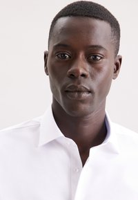 Witte overhemden met klassieke kraag en zichtbare stiksels. Glad stof, aansluitend ontwerp en subtiele accentkleur aan de binnenkant van de kraag.