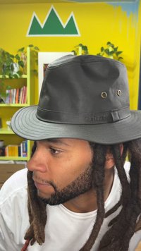 Černý voděodolný klobouk s širokou krempou, ozdobený páskem a jemným logem. Hladký povrch s dvěma větracími otvory na boku.