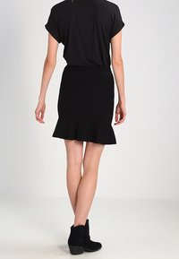 Černý krátký top s krátkými rukávy spojený s přiléhavou černou sukní s rozšířeným lemem, vyrobenou z hladké látky, doplněný černými kotníkovými botami.