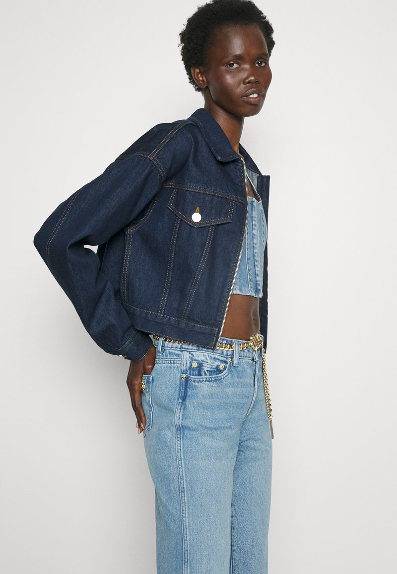 Ciemnoniebieska kurtka dżinsowa o krótkim kroju, zapinana na guziki, z bocznymi kieszeniami. W połączeniu z jasnoniebieskimi dżinsami z dodatkami w kolorze złotym.