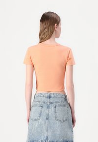T-shirt orange à manches courtes, crop, avec un col rond et un tissu lisse, associé à une jupe en denim taille haute ornée d'un motif logo discret.