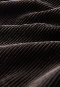 Gros plan d'un tissu en velours côtelé brun foncé montrant des nervures et plis doux et texturés avec une lumière et une ombre variées.
