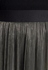 Falda negra plisada con detalles de hilo metálico. Presenta una ancha cinturilla negra con el logotipo "HUGO" en un diseño sutil y tonal.