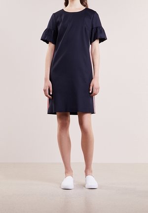 Vestito blu navy con maniche corte a volant, scollatura rotonda e strisce laterali. Indossato con scarpe bianche slip-on, design minimalista.