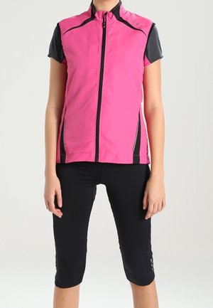 Femme portant un gilet de cyclisme rose sans manches avec des panneaux latéraux noirs par-dessus un t-shirt noir à manches courtes et des leggings noirs courts.