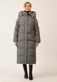 Dunkelgraue Pufferjacke mit hohem Kragen, gestepptem Design und Reißverschluss. Verfügt über lange Ärmel und Taschen. Kombiniert mit knielangen schwarzen Stiefeln.