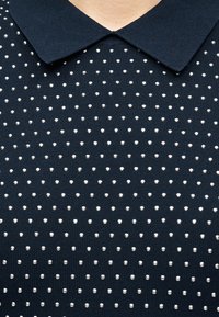 Μπλε ναυτικό πλεκτό πουκάμισο με μυτερό γιακά, διακοσμημένο με μικρές ασημί καρφίτσες, τοποθετημένες ομοιόμορφα σε οριζόντιες σειρές.