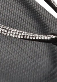 Chancla negra con una suela texturizada y una correa adornada con strass transparentes para un detalle decorativo.