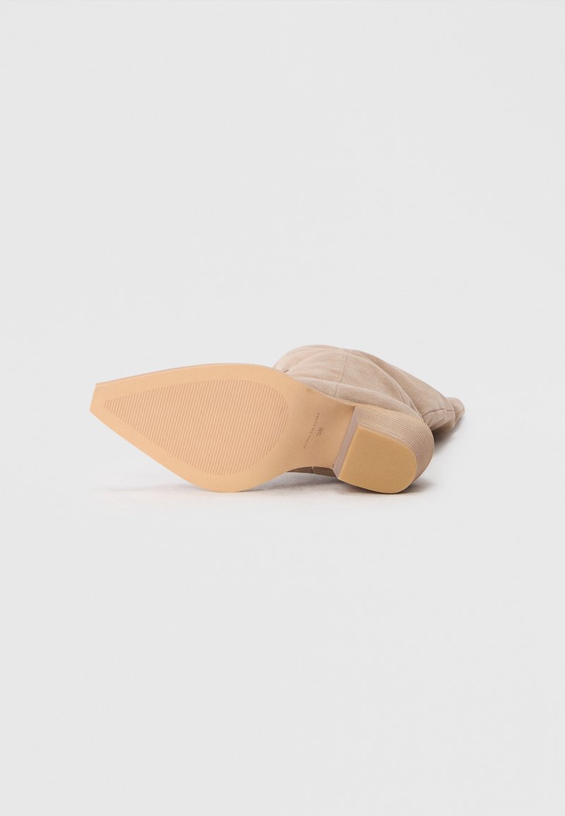 Botín de ante beige con punta redondeada, tacón bajo apilado y suela de goma texturizada con estrías horizontales para mayor tracción.