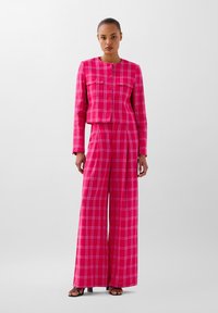 Conjunto de dos piezas a cuadros rosa que incluye una chaqueta corta con botones y pantalones de pierna ancha. Textura suave con detalles en patrón de cuadros.