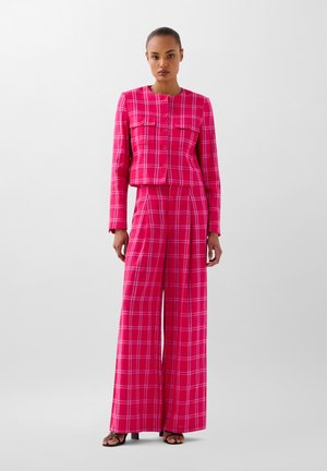 Růžový károvaný dvoudílný outfit obsahující zkrácenou bundu s knoflíky a široké kalhoty. Měkká textura s detaily kostičkovaného vzoru.