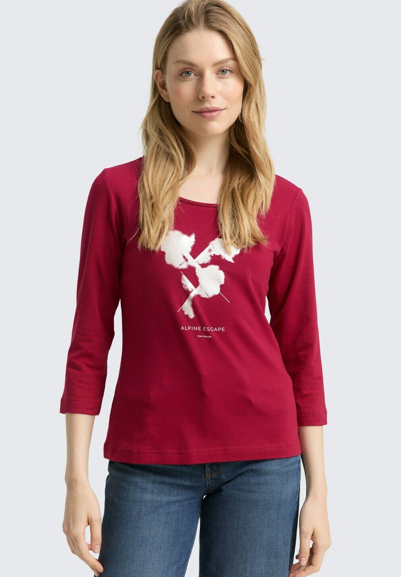 Rotes Langarmshirt mit einem weißen Berggrafik und dem Text "ALPINE ESCAPE." Weicher Stoff mit quadratischem Ausschnitt und lockerer Passform.