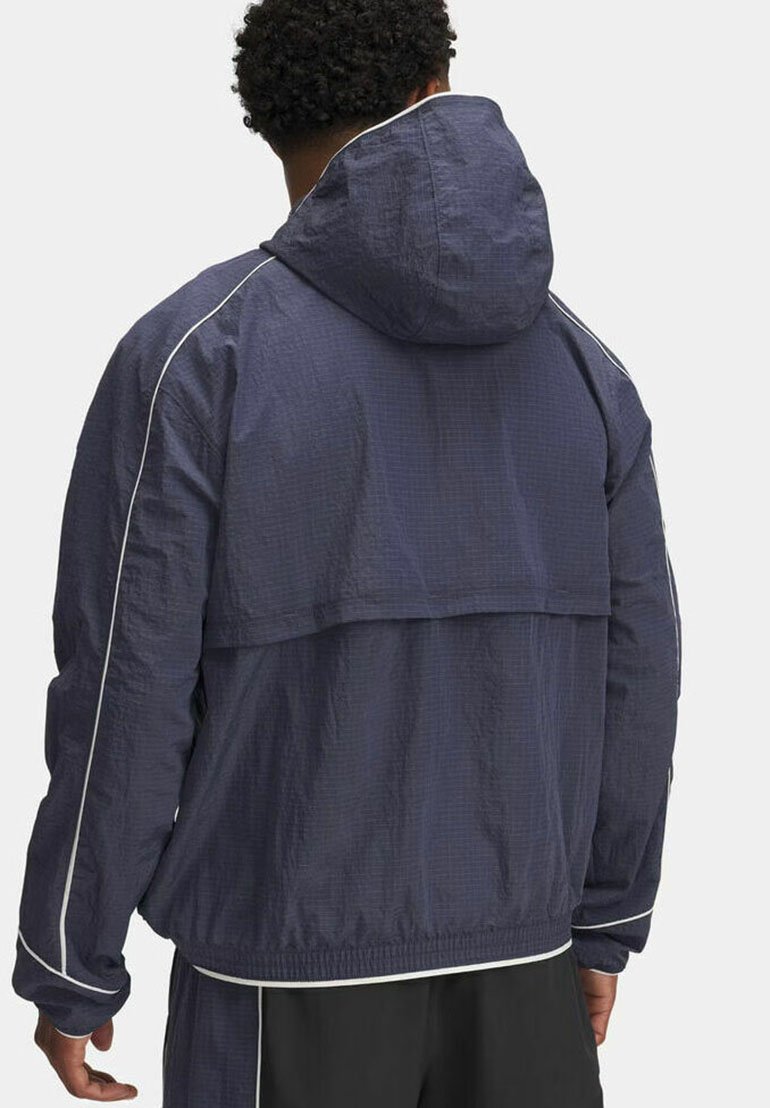 Veste coupe-vent marine avec capuche, présentant une surface texturée, des garnitures blanches et une coupe ample. Manches élastiques et ourlet élastique.