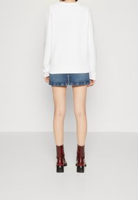 Sudadera blanca con puños y dobladillo acanalados, combinada con una mini falda vaquera y botines burdeos con tacón de bloque.