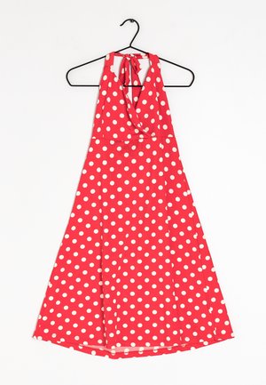 Vestido rojo con cuello halter y lunares blancos, con diseño envolvente, tela fluida y un lazo en el cuello. Cuelga de una percha negra.
