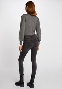 Szary top z bufiastymi rękawami w połączeniu z czarnymi, wysokimi skinny jeansami i czarnymi botkami za kostkę, widok z tyłu. Gładka faktura materiału.