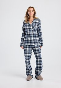 Flannel pajama set in navy and white plaid, featuring long sleeves, button closure, chest pocket, and relaxed-fit pants with matching pattern.